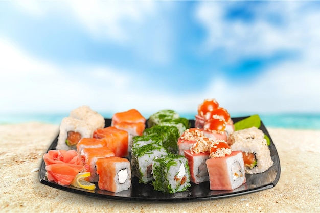 Tasty Sushi rolls on plate on beach background