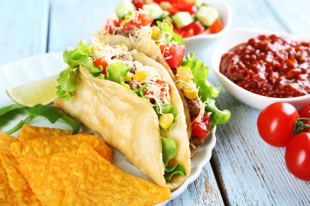 Tasty taco with nachos chips and vegetables on plate on table close up