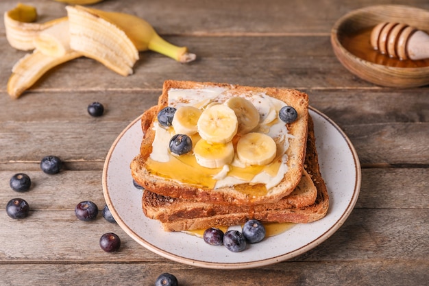 Tasty toasted bread with honey, butter and fruits on plate