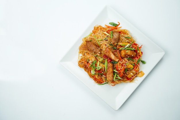 Tasty udon noodles in sweet and sour sauce with vegetables and pork meat plate on a gray table. Top view with copy space