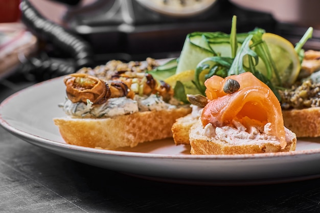 Tasty various italian sandwiches with seafood against rustic wooden background. Crostini with cheese, red fish, lemon and sliced olives, horizontal view with selective focus