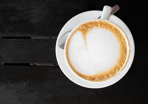 Tasty white cup of cappuccino with latte art on wooden table