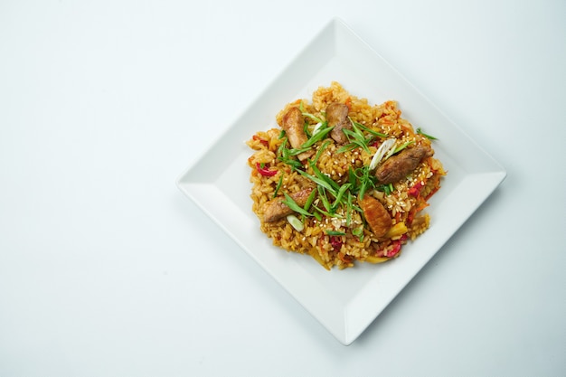 Tasty wok rice in sweet and sour sauce with vegetables and beef in a white plate on a gray table. Top view with copy space