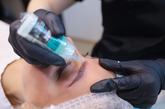 The tattoo artist applies a drop of anesthesia to the client's eyebrows