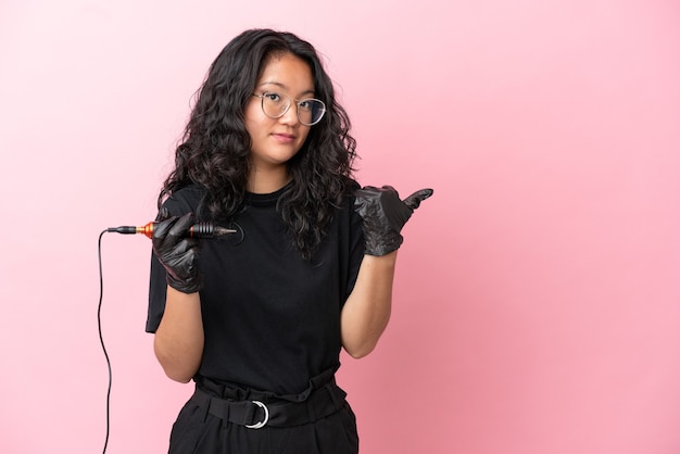 Tattoo artist asian woman isolated on pink background pointing to the side to present a product