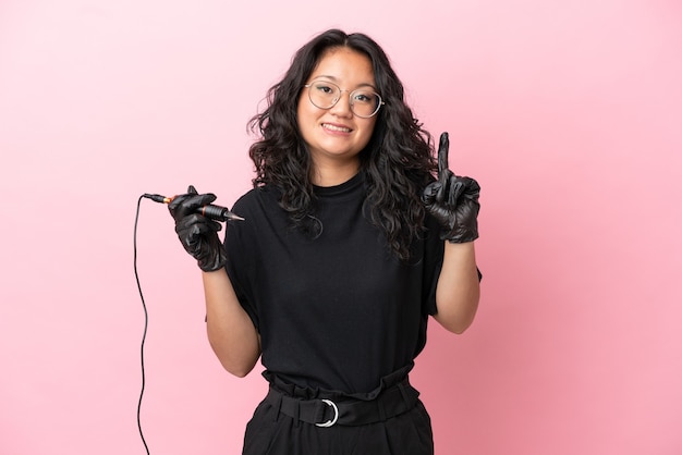 Tattoo artist asian woman isolated on pink background showing and lifting a finger in sign of the best