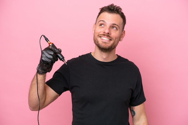 Tattoo artist brazilian man isolated on pink background thinking an idea while looking up