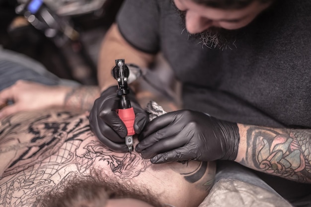 Tattoo artist demonstrates the process of getting tattoo in tattoo parlour./Tattoo master posing in the salon.