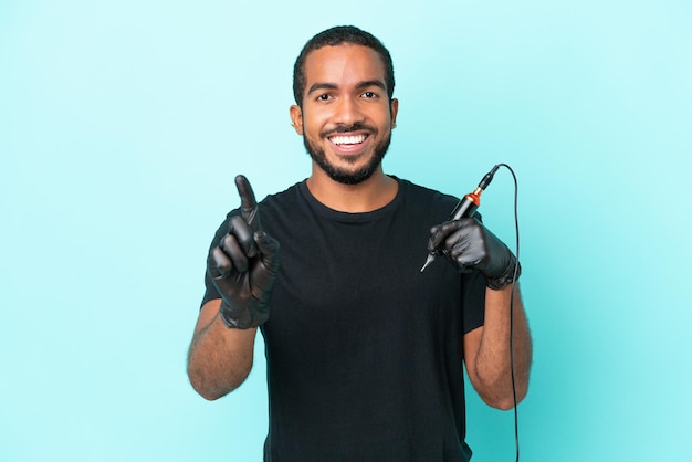 Tattoo artist Ecuadorian man isolated on blue background showing and lifting a finger