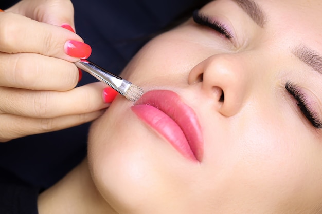 The tattoo artist holds a brush in his hand and smears a foundation near his lips correcting the finished tattoo work