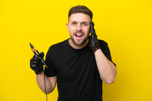 Tattoo artist man isolated on yellow background with surprise and shocked facial expression