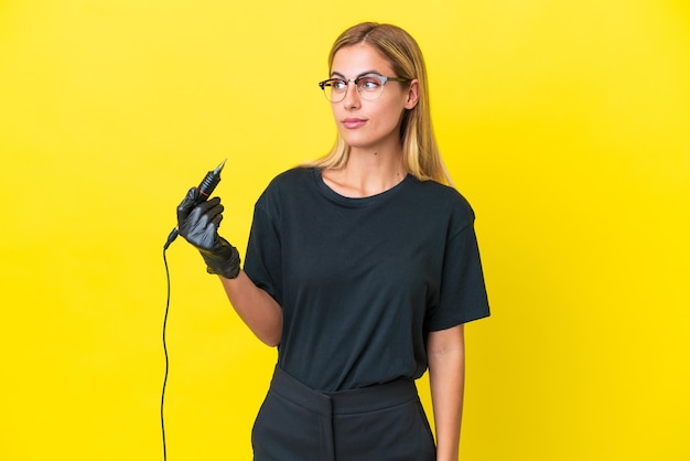 Tattoo artist Uruguayan woman isolated on yellow background looking to the side