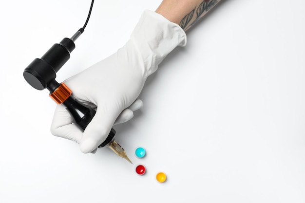 Tattoo artist with professional machine and colorful ink on white background top view