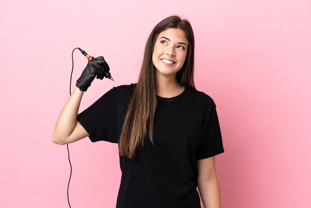 Tattoo artist woman isolated on pink background thinking an idea while looking up