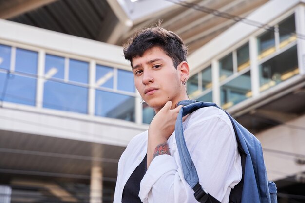 Tattooed man in shirt with a backpack on his shoulder looking at the camera