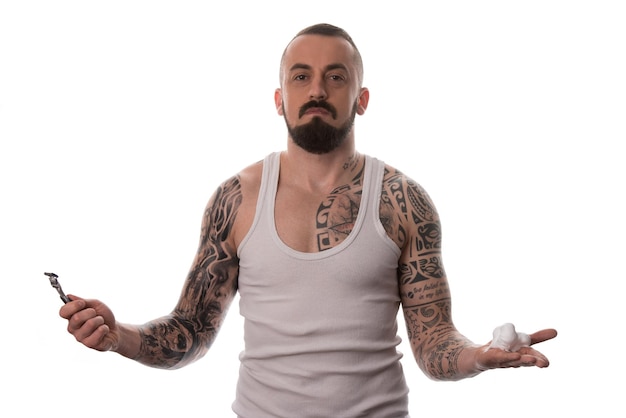 Photo tattooed man styling beard holding disposable razor  isolated on white background