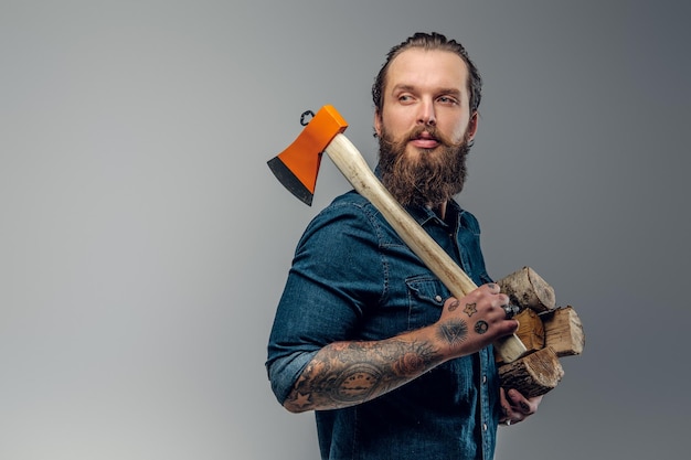 Tattooed man with firewood and axe in hands is posing for photographer.