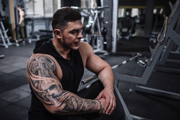 Tattooed muscular male athlete looking focused, preparing to workout at the gym