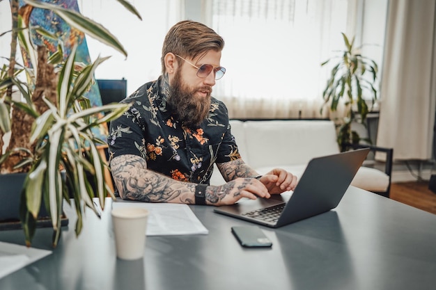 Tattooed and serious business hipster doing his job on a laptop