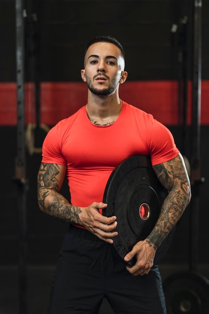 tattooed young guy doing sports in a gym with weights and rowing machine