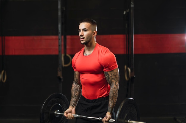 tattooed young guy doing sports in a gym with weights and rowing machine