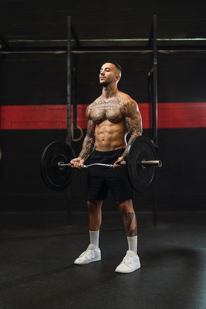 tattooed young guy doing sports in a gym with weights and rowing machine