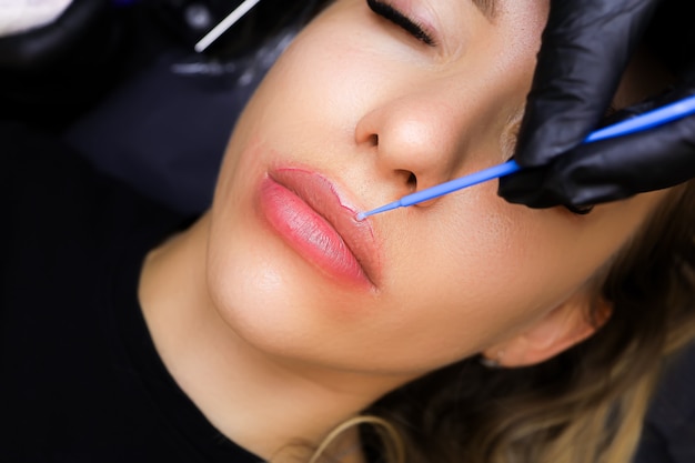 The tattooist applies anesthesia to the contour of the model's lips with a small brush