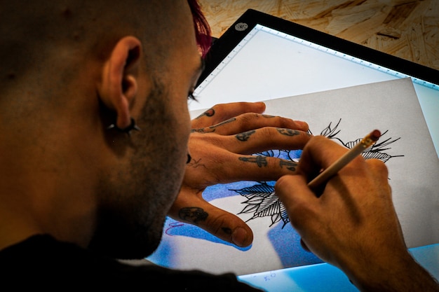 Tattooist designing a tattoo drawing on paper on a digital drawing tablet in his tattoo studio