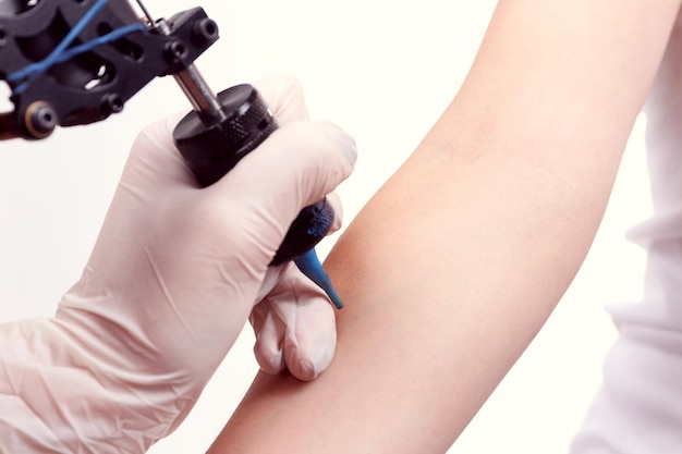 Tattooist draws on the woman's arm on white background close up