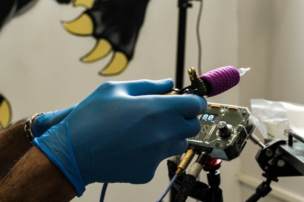 Tattooist with blue latex gloves preparing the needle and the tattoo machine.