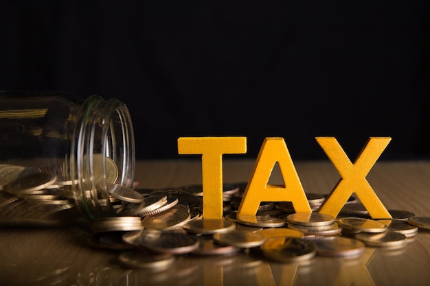 Tax Concept. Word tax put on coins and glass bottles with coins inside on black background.