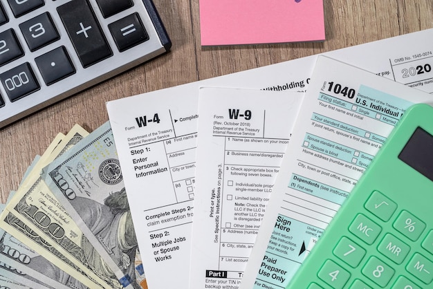 Tax forms 1040 are blank to fill out and dollars are sloppily scattered on a wooden table