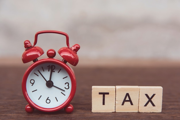 Tax with wooden alphabet blocks, Red alarm clock on dark plank wooden with copy space