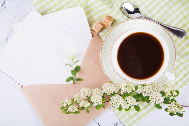 Tea in a beautiful white cup. A kraft mail envelope with sheets of paper. Breakfast. A branch of flowering spirea. Japanese concept wabi sabi