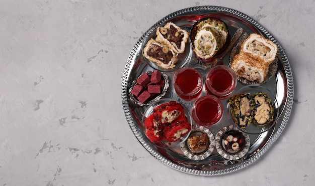 tea ceremony with an assortment of turkish sweets on a round metal tray on a gray background