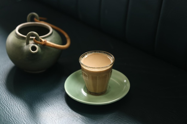 Tea concept - a hot, steaming cup of tea with a teapot, on a black background.