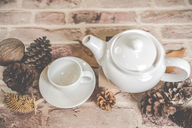 Tea concept white teapot with white tea cup with dry leaves on wooden background