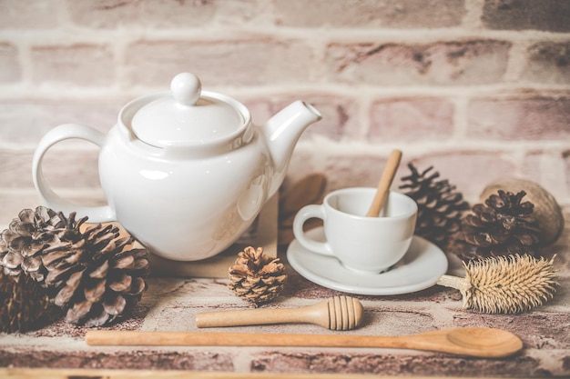 Tea concept white teapot with white tea cup with dry leaves on wooden background