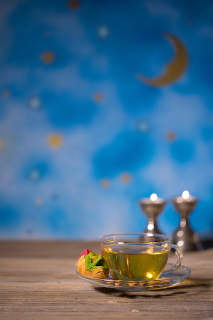 Tea in a glass cup with Arabic sweets on a wooden surface Night blue sky in the background