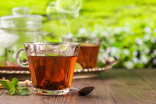 Tea in a glass cup on the wooden table and the tea plantations background