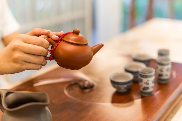 Tea is poured into the cup closeup. Asian tea set-up on wooden bamboo table, hand gently pouring