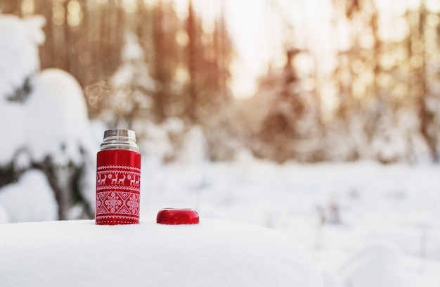 Tea in red thermos in winter forest