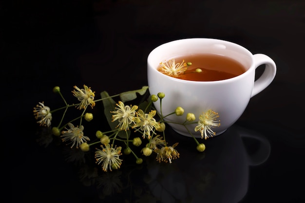 Tea in a white cup with a linden on a black background with reflection