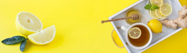 Tea with lemon honey and ginger on the white wooden tray on the yellow background Copy space Top view