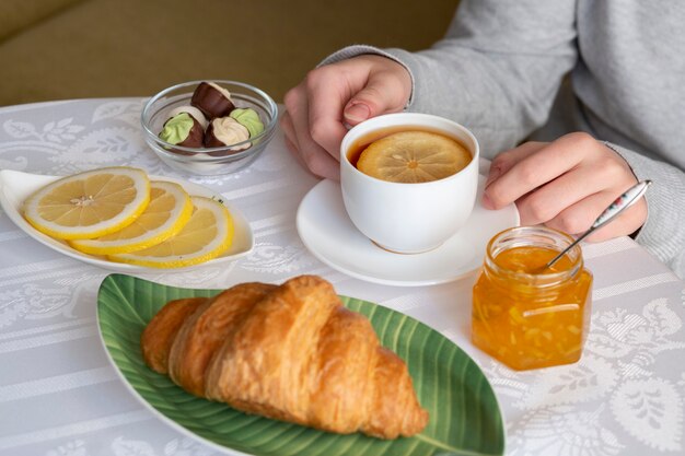 Tea with lemon, jam, croissant and chocolates on a white table