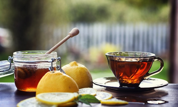 Tea with lemon and mint in nature. A cup of hot mint tea with lemon and honey in jar. Lemon slices and a spoon with honey to hot tea.