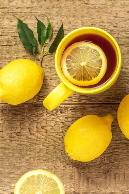 Tea with lemon in a yellow mug on a wooden background and fresh lemonCopy space for textTop view