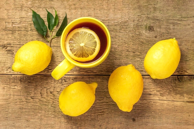 Tea with lemon in a yellow mug on a wooden background and fresh lemonsCopy space for textTop view