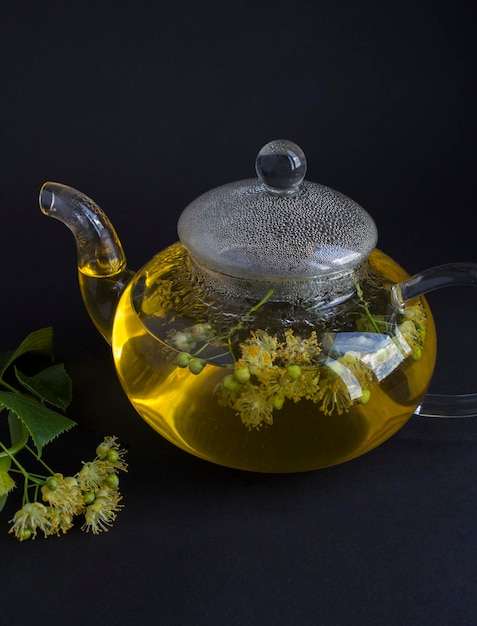 Tea with linden flower in the glass teapotn on the black background Location vertical