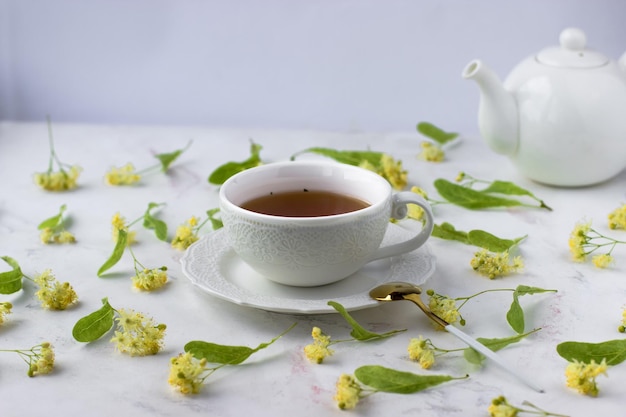 Tea with linden in a white cup on a white marble table White teapot with aromatic tea